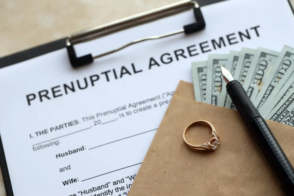 Prenuptial agreement form with money, engagement ring, and pen on table, symbolizing financial and legal preparation before marriage.