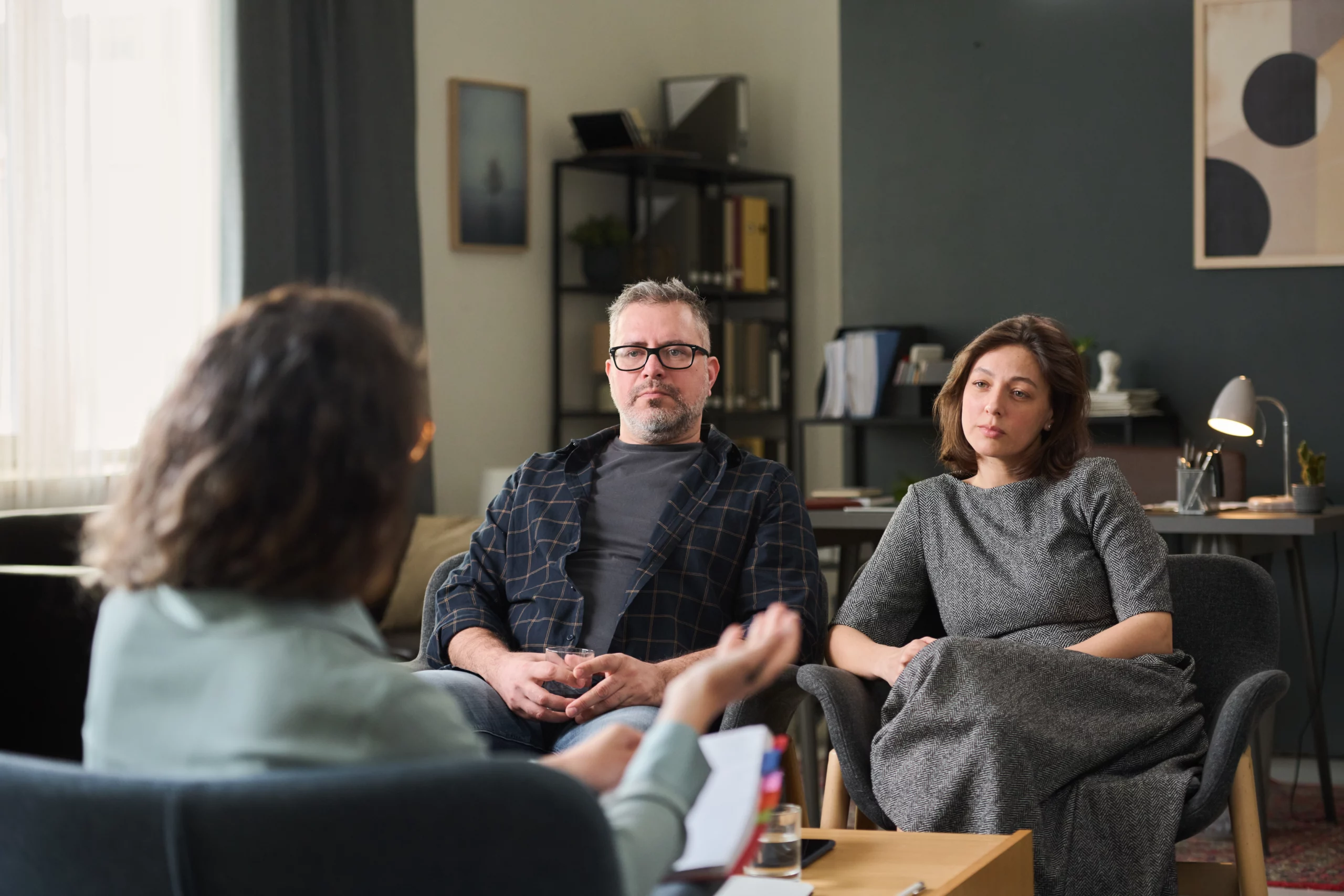 A couple attentively listening to a therapist in a cozy, softly lit room, discussing child custody modifications in a supportive setting.