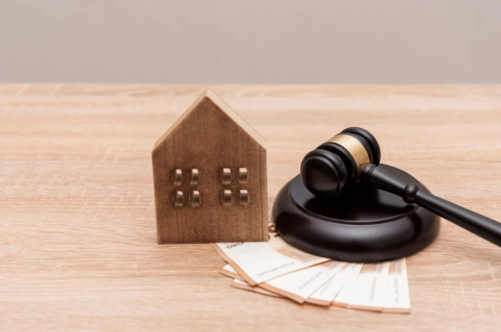 Wooden gavel beside Euro banknotes and a house model, representing probate and real estate law.