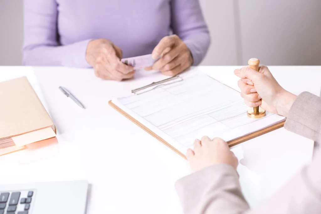 Two people reviewing and stamping legal documents with ID and clipboard at desk, representing estate planning process of choosing between a trust and a will in Houston