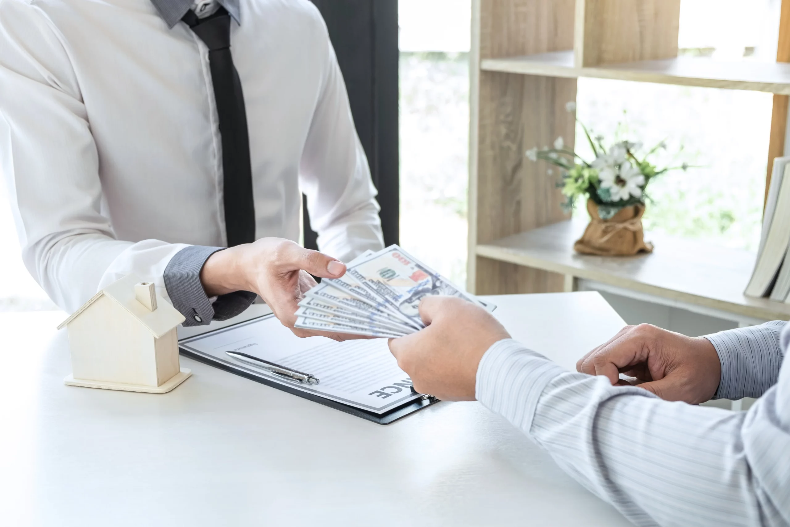 Two people exchanging cash over lease agreement with model house on desk, representing rent payments and Texas landlord late fee laws on what fees can legally be charged